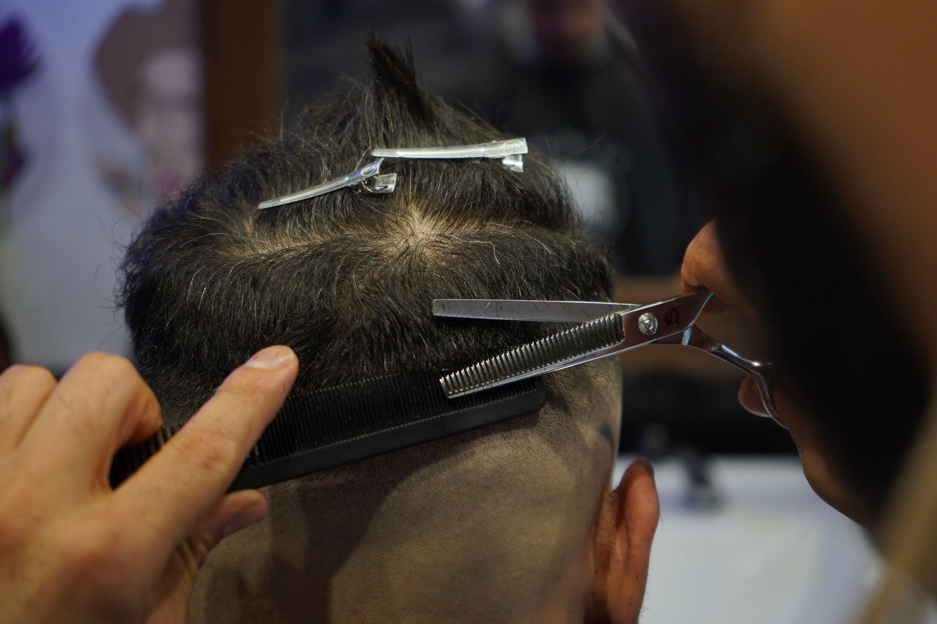 Close-up of a barber skillfully cutting a customer's hair with scissors and a comb indoors.